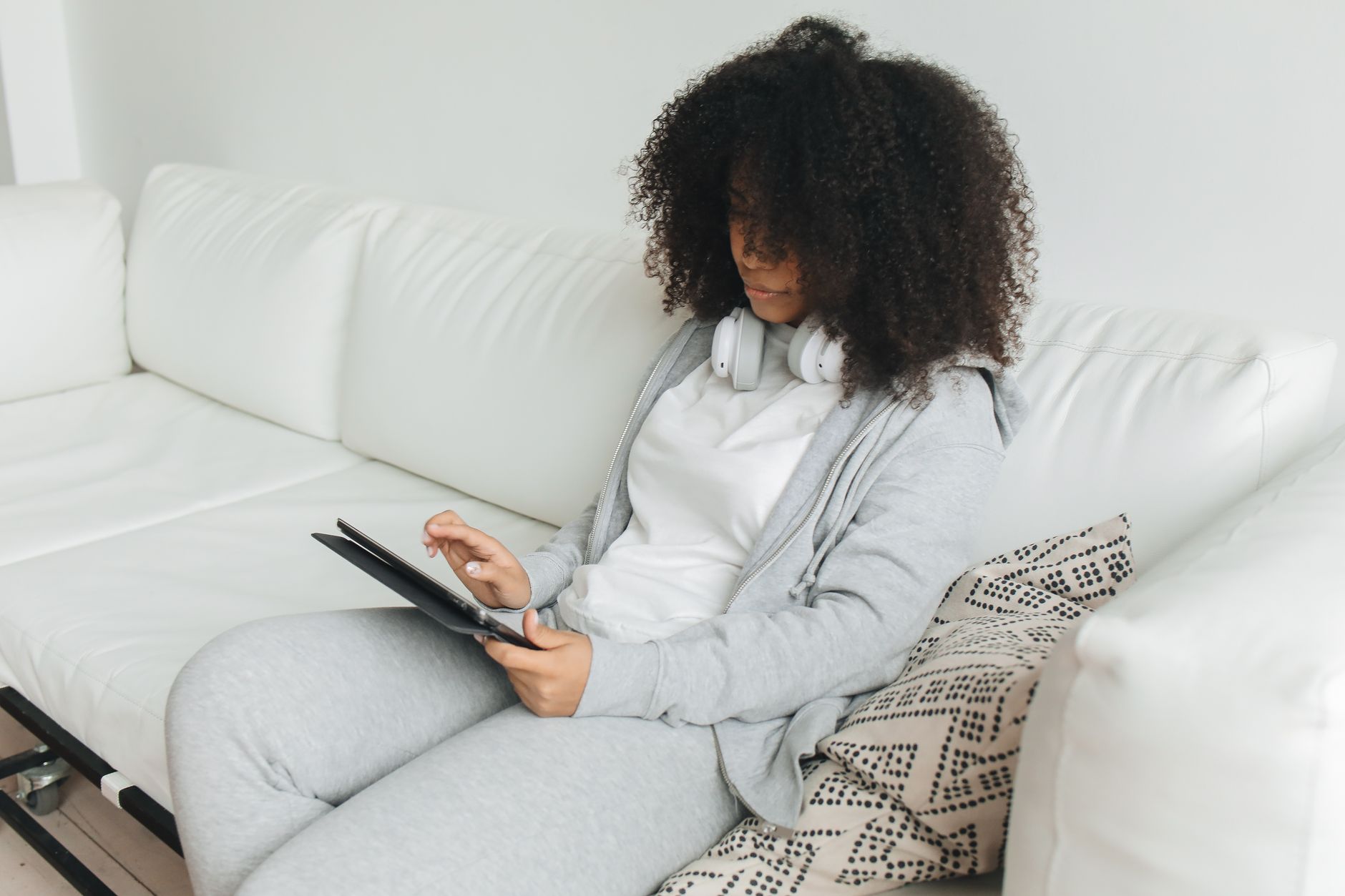 Vrouw met koptelefoon gebruikt een tablet op een witte bank
