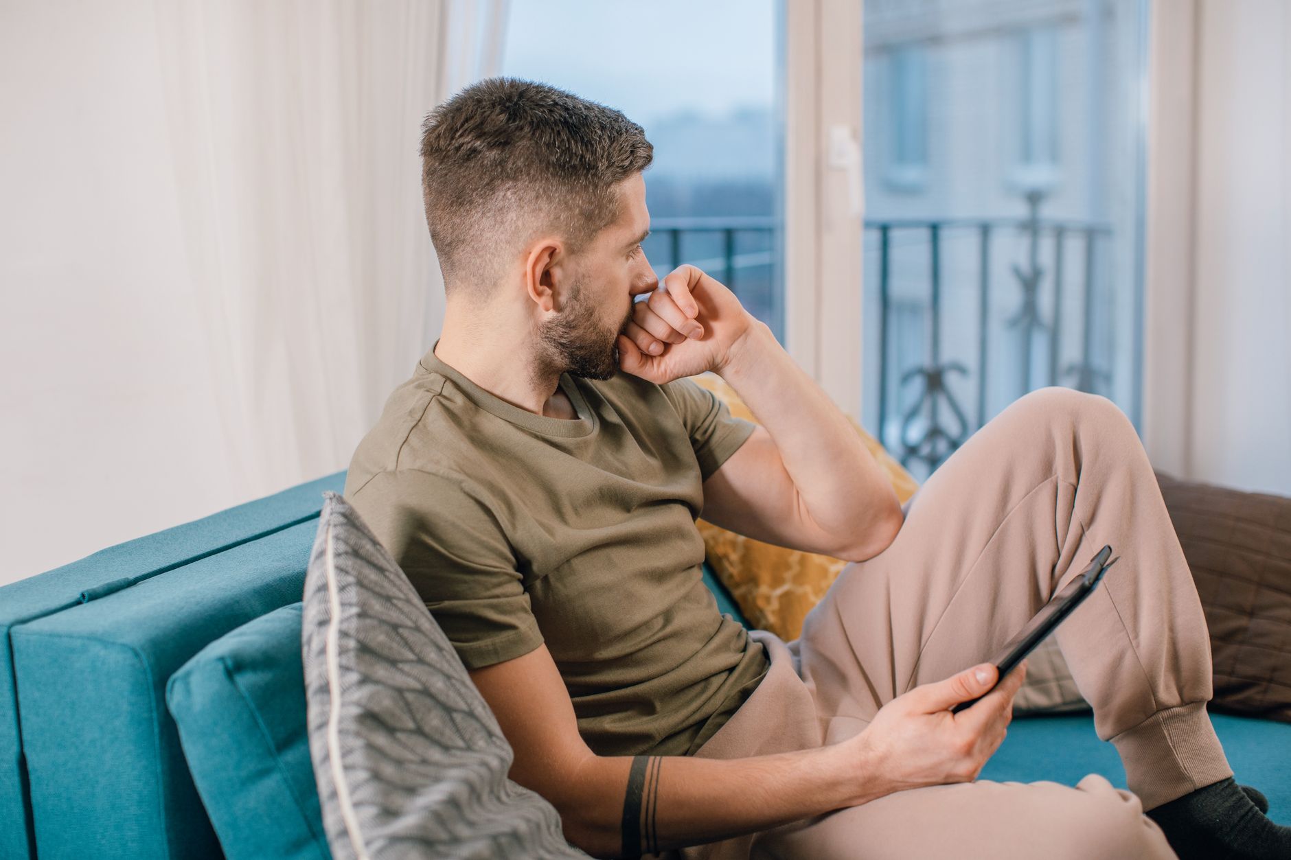 Man met baard zit peinzend op de bank binnenshuis met een tablet in zijn handen